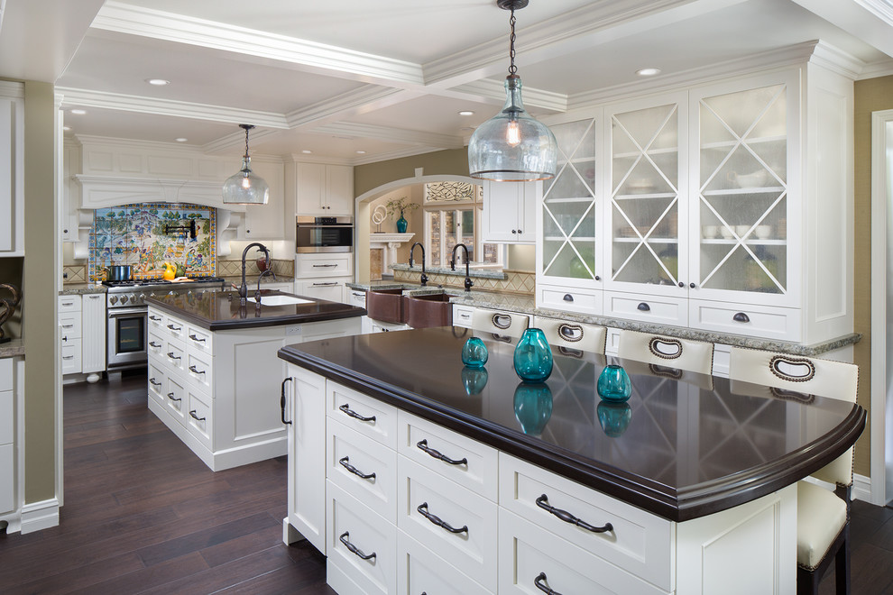 Photo of a mid-sized transitional u-shaped open plan kitchen in Orange County with a farmhouse sink, white cabinets, quartz benchtops, stainless steel appliances, dark hardwood floors, multiple islands, shaker cabinets, ceramic splashback, multi-coloured splashback, brown floor and brown benchtop.