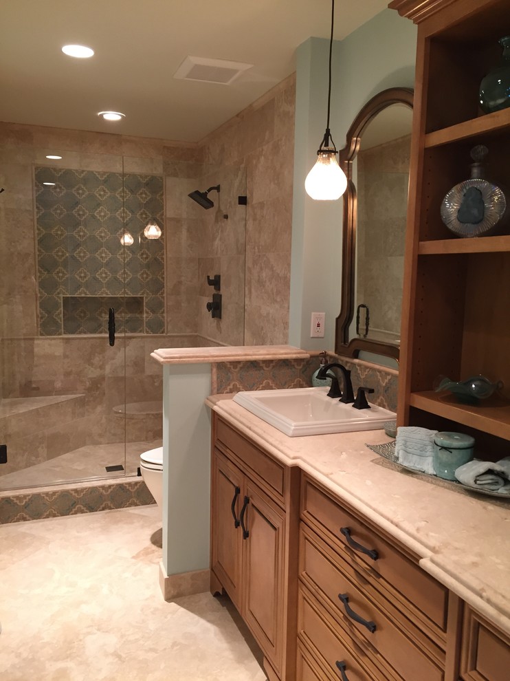 Design ideas for a mid-sized mediterranean 3/4 bathroom in Los Angeles with raised-panel cabinets, medium wood cabinets, an alcove shower, a one-piece toilet, beige tile, limestone, blue walls, limestone floors, a drop-in sink, limestone benchtops, beige floor and a hinged shower door.