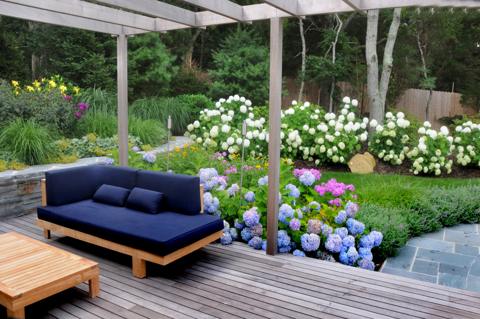 This is an example of a mid-sized country backyard partial sun garden in New York with a retaining wall and decking.