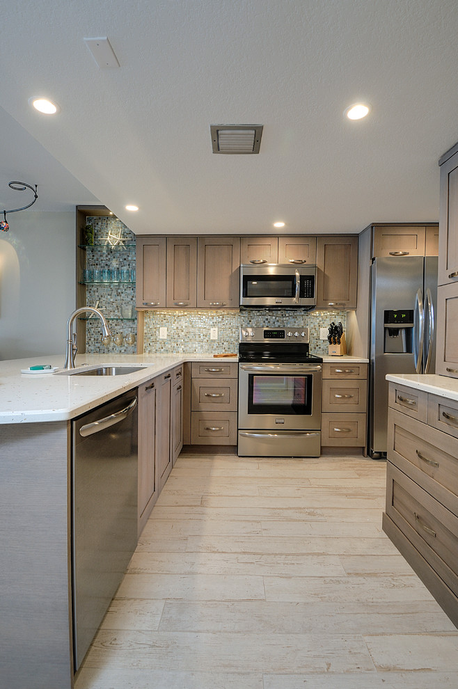 Design ideas for a mid-sized beach style l-shaped open plan kitchen in Tampa with an undermount sink, shaker cabinets, grey cabinets, quartz benchtops, blue splashback, glass tile splashback, stainless steel appliances, porcelain floors and a peninsula.