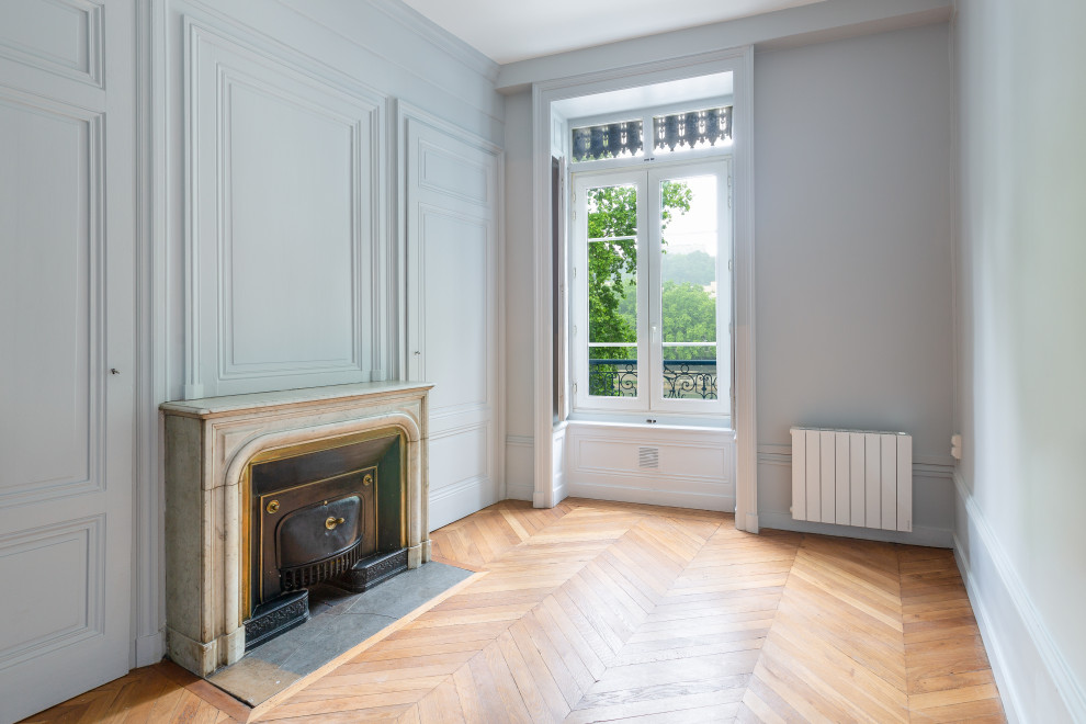 Mittelgroßes, Abgetrenntes Klassisches Wohnzimmer mit blauer Wandfarbe, hellem Holzboden, Kamin und braunem Boden in Lyon
