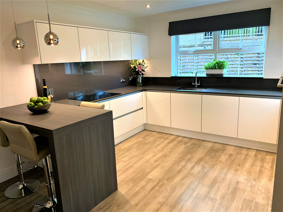 Inspiration for a small contemporary u-shaped separate kitchen in Other with a single-bowl sink, flat-panel cabinets, medium wood cabinets, solid surface benchtops, grey splashback, stainless steel appliances, vinyl floors, a peninsula and grey benchtop.