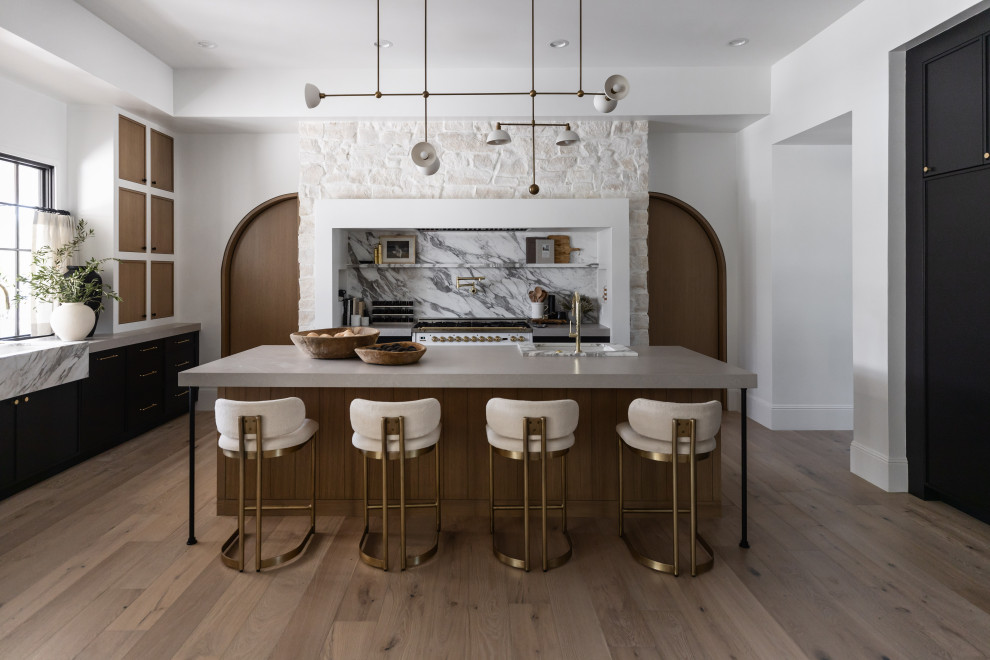 Inspiration for a transitional l-shaped medium tone wood floor and brown floor kitchen remodel in Phoenix with an undermount sink, black cabinets, white backsplash, stone slab backsplash, white appliances, an island and gray countertops