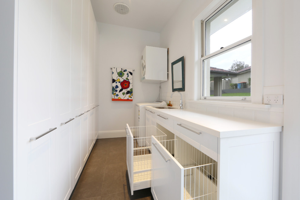 Contemporary galley laundry room in Melbourne with shaker cabinets, white cabinets, white walls, a stacked washer and dryer and a single-bowl sink.