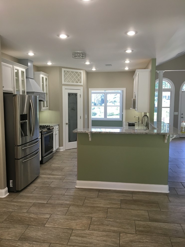 Design ideas for a mid-sized transitional u-shaped kitchen in Charleston with recessed-panel cabinets, white cabinets, stainless steel appliances, porcelain floors, with island and brown floor.