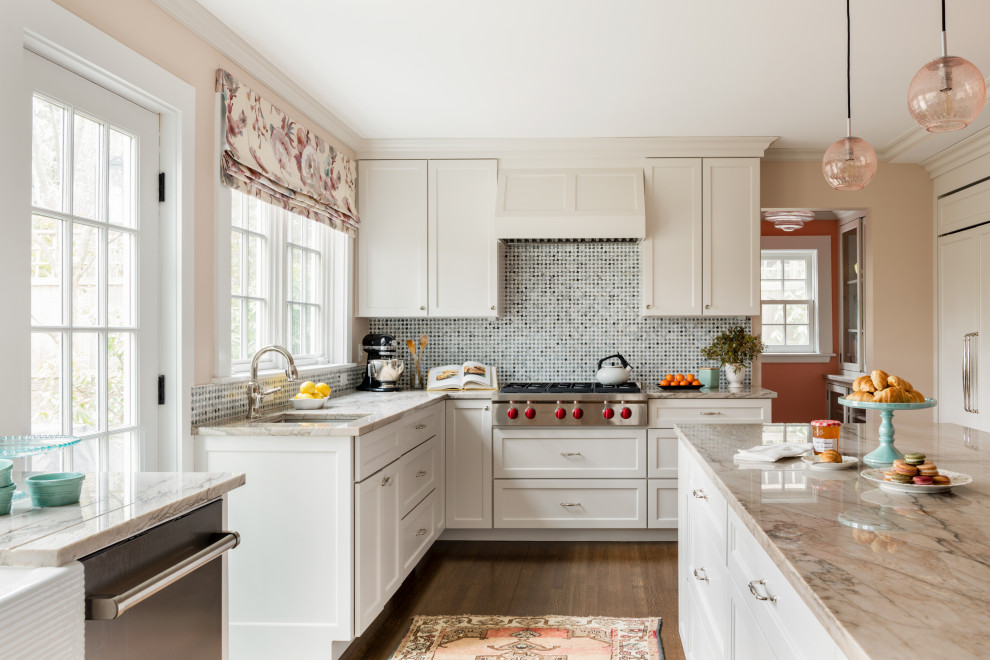 Mid-sized transitional l-shaped eat-in kitchen in Boston with a farmhouse sink, flat-panel cabinets, white cabinets, granite benchtops, multi-coloured splashback, mosaic tile splashback, stainless steel appliances, medium hardwood floors, with island, brown floor and grey benchtop.