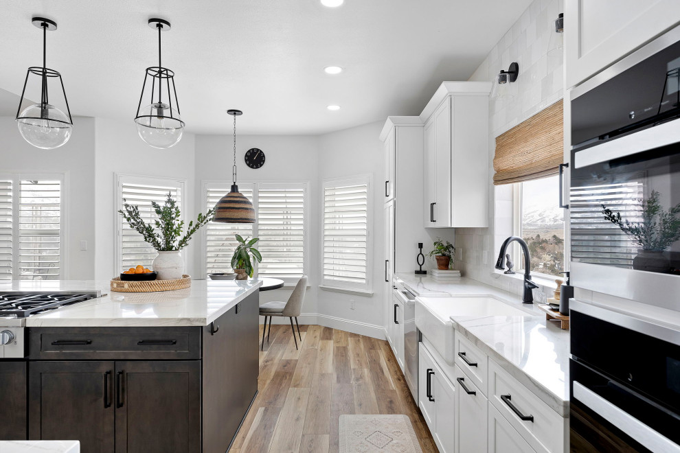 Example of a transitional vinyl floor and brown floor kitchen design with a farmhouse sink, shaker cabinets, white cabinets, quartzite countertops, white backsplash and stainless steel appliances