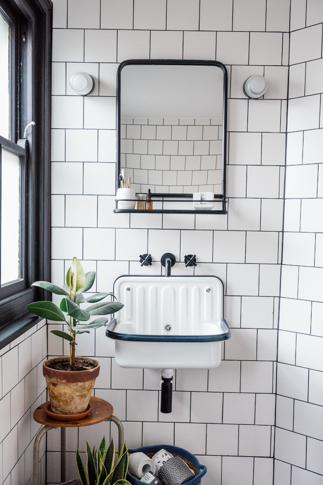 Inspiration for a mid-sized scandinavian kids bathroom in Kent with a drop-in tub, a shower/bathtub combo, a one-piece toilet, white tile, ceramic tile, white walls, terrazzo floors, a wall-mount sink, black floor, a hinged shower door and a single vanity.