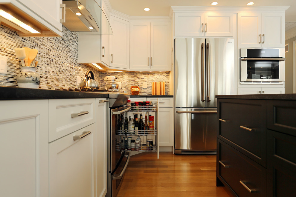Inspiration for a mid-sized transitional l-shaped light wood floor open concept kitchen remodel in Boston with white cabinets, granite countertops, an island, an undermount sink, shaker cabinets, gray backsplash, matchstick tile backsplash and stainless steel appliances