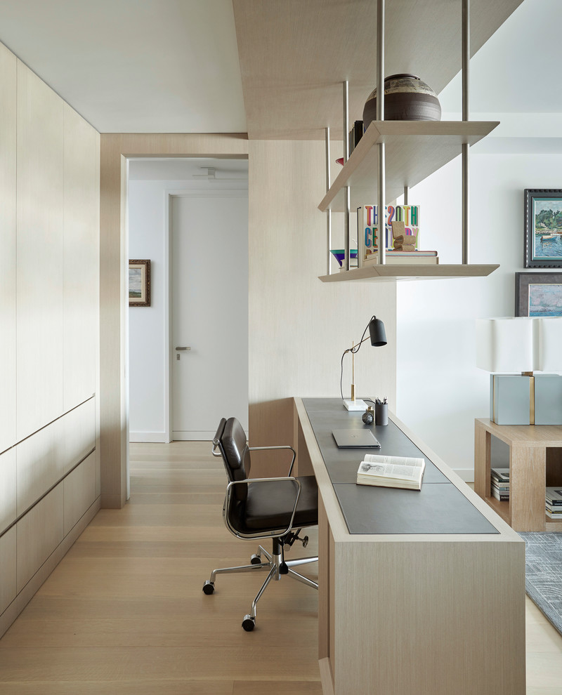Photo of a contemporary home office in New York with white walls, light hardwood floors, a built-in desk and beige floor.