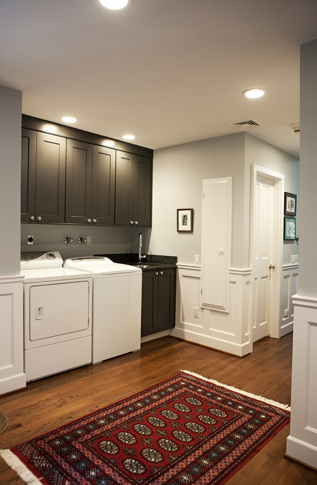 This is an example of a traditional single-wall dedicated laundry room in New York with an undermount sink, shaker cabinets, grey cabinets, granite benchtops, grey walls and a side-by-side washer and dryer.