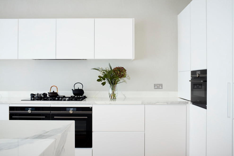 Design ideas for a mid-sized contemporary l-shaped open plan kitchen in London with an undermount sink, louvered cabinets, white cabinets, marble benchtops, white splashback, marble splashback, panelled appliances, with island and white benchtop.