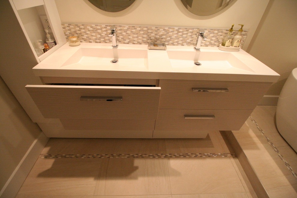Photo of a large contemporary master bathroom in Montreal with flat-panel cabinets, beige cabinets, a freestanding tub, a one-piece toilet, beige tile, porcelain tile, beige walls, porcelain floors and an integrated sink.
