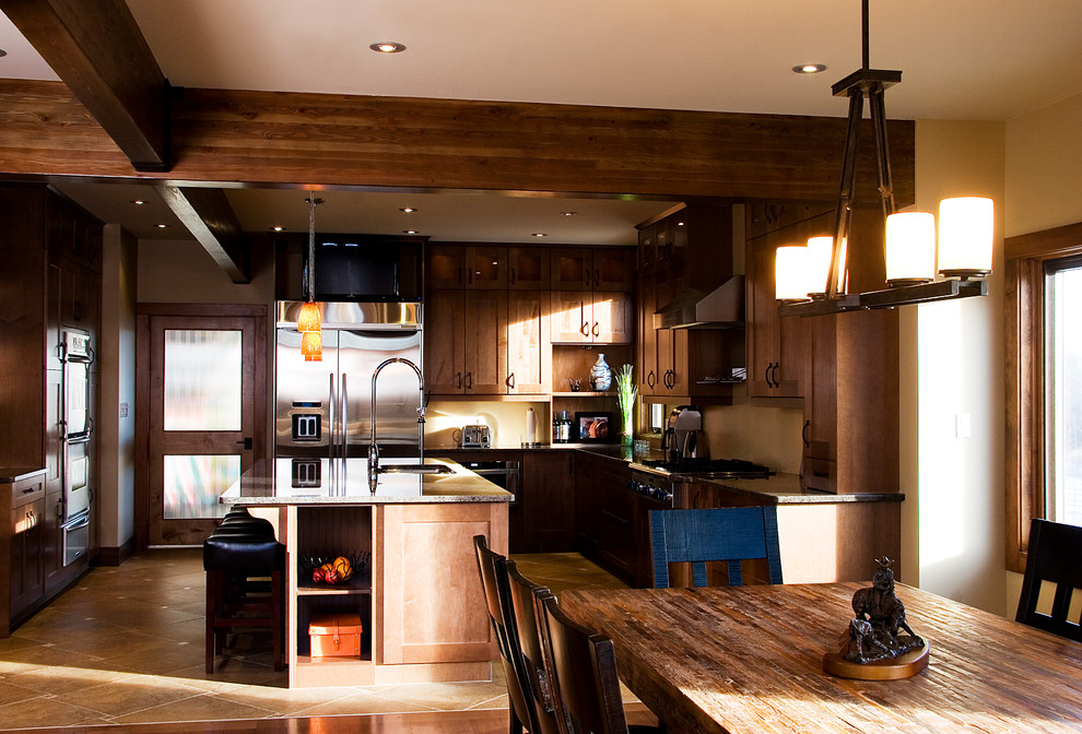 Example of a mid-sized mountain style u-shaped travertine floor enclosed kitchen design in Edmonton with an undermount sink, shaker cabinets, brown cabinets, granite countertops and an island