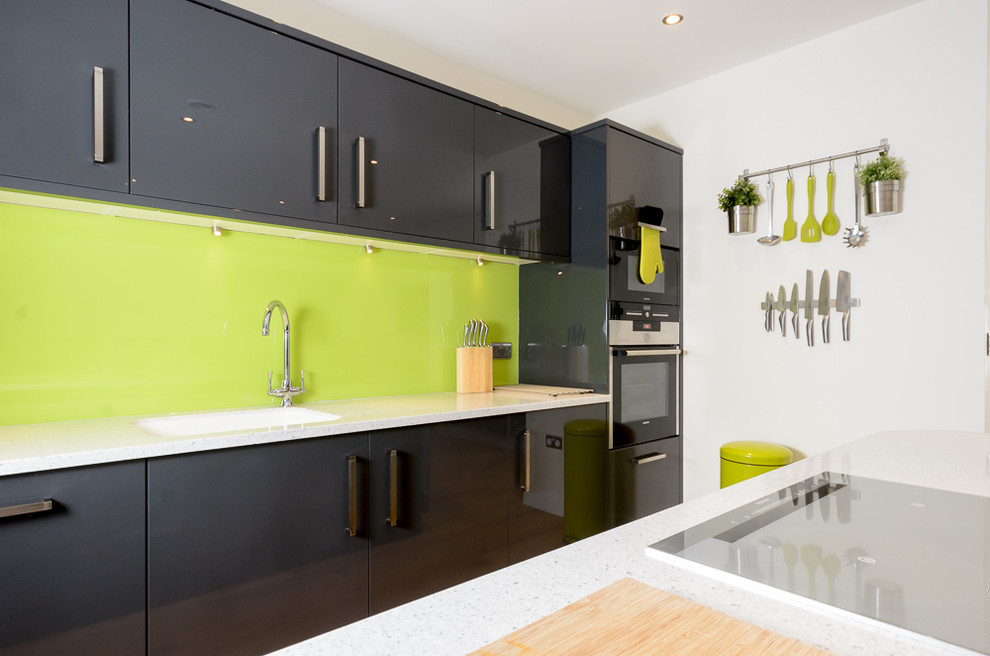 Photo of a modern single-wall eat-in kitchen in Other with a drop-in sink, flat-panel cabinets, grey cabinets, solid surface benchtops, green splashback, glass sheet splashback, panelled appliances, vinyl floors and with island.