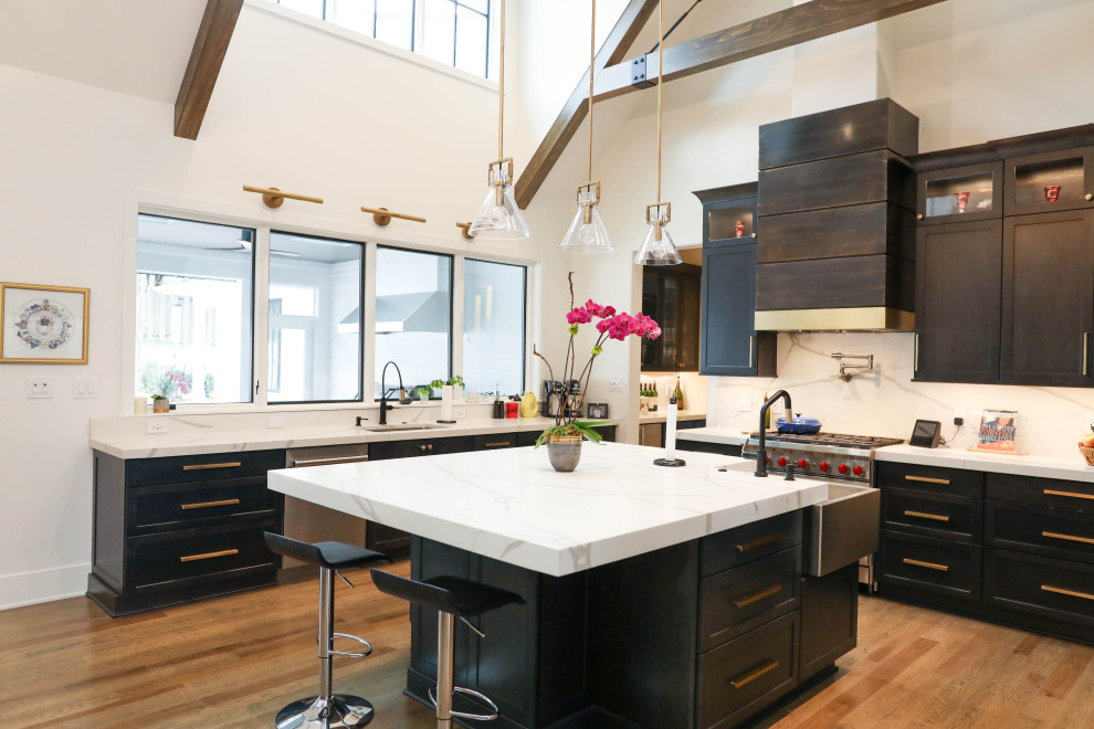 Open concept kitchen - large transitional u-shaped light wood floor open concept kitchen idea with a farmhouse sink, flat-panel cabinets, dark wood cabinets, quartz countertops, white backsplash, quartz backsplash, stainless steel appliances, an island and white countertops