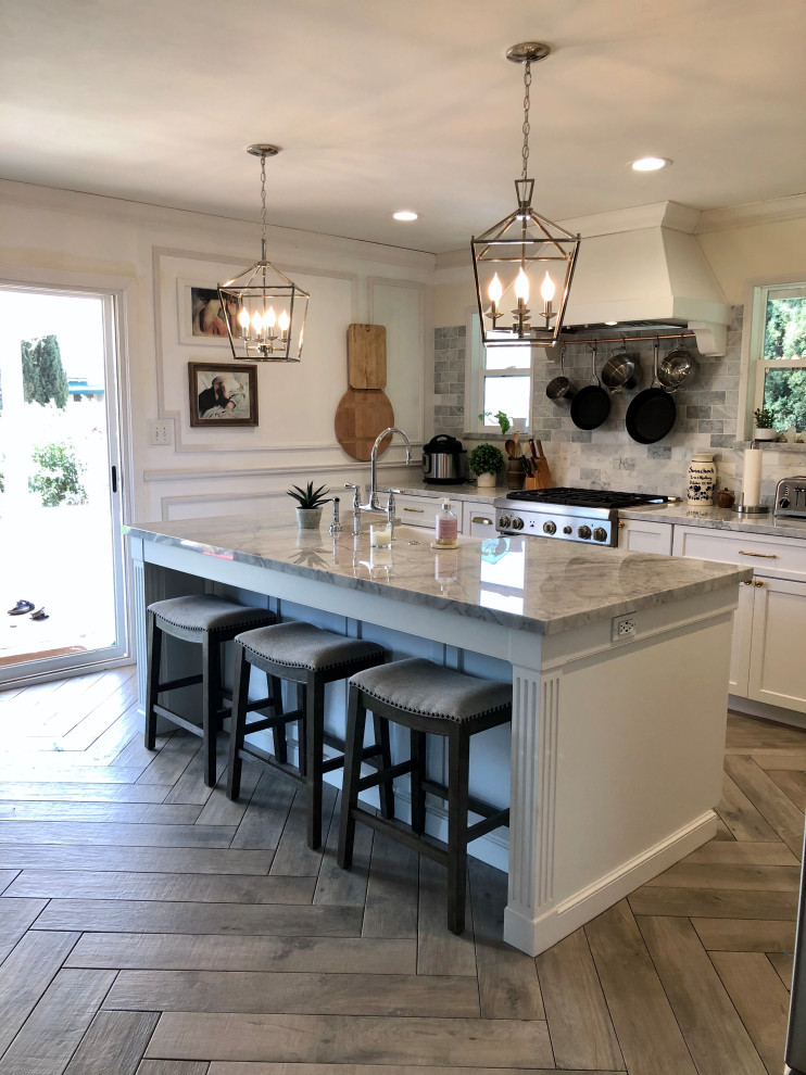 Inspiration for a mid-sized traditional l-shaped eat-in kitchen in Santa Barbara with a farmhouse sink, shaker cabinets, white cabinets, marble benchtops, white splashback, marble splashback, stainless steel appliances, porcelain floors, with island, brown floor and multi-coloured benchtop.