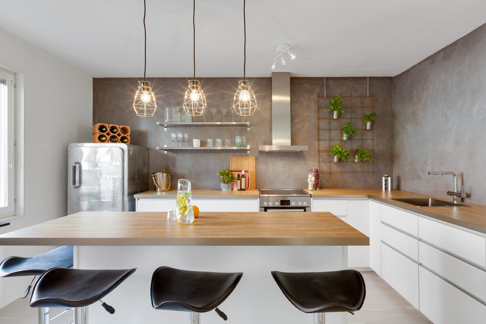 This is an example of a mid-sized contemporary l-shaped kitchen in Stockholm with a single-bowl sink, flat-panel cabinets, white cabinets, grey splashback, stainless steel appliances, with island, wood benchtops and light hardwood floors.