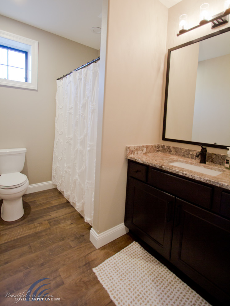 This is an example of a mid-sized traditional bathroom in Other with recessed-panel cabinets, dark wood cabinets, a shower/bathtub combo, a two-piece toilet, beige walls, vinyl floors, an undermount sink, engineered quartz benchtops, brown floor, a shower curtain, beige benchtops, a single vanity and a built-in vanity.