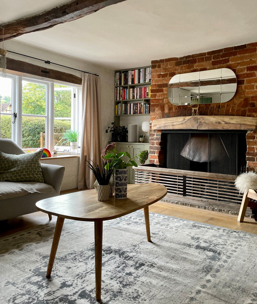 Small contemporary enclosed living room in Hertfordshire with white walls, light hardwood flooring, a standard fireplace, a brick fireplace surround, a freestanding tv, brown floors, exposed beams, brick walls and a chimney breast.