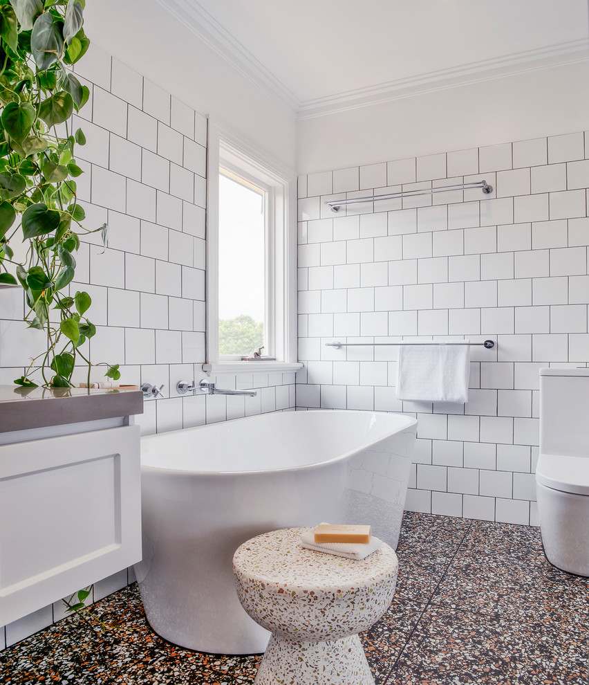 Photo of a mid-sized modern 3/4 bathroom in Melbourne with shaker cabinets, white cabinets, a freestanding tub, a curbless shower, a two-piece toilet, white tile, ceramic tile, white walls, terrazzo floors, a drop-in sink, engineered quartz benchtops, black floor, an open shower and grey benchtops.