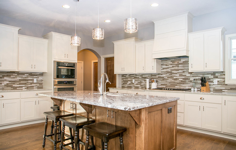 Inspiration for a transitional u-shaped medium tone wood floor open concept kitchen remodel in Minneapolis with an undermount sink, shaker cabinets, white cabinets, granite countertops, multicolored backsplash, ceramic backsplash, stainless steel appliances and an island