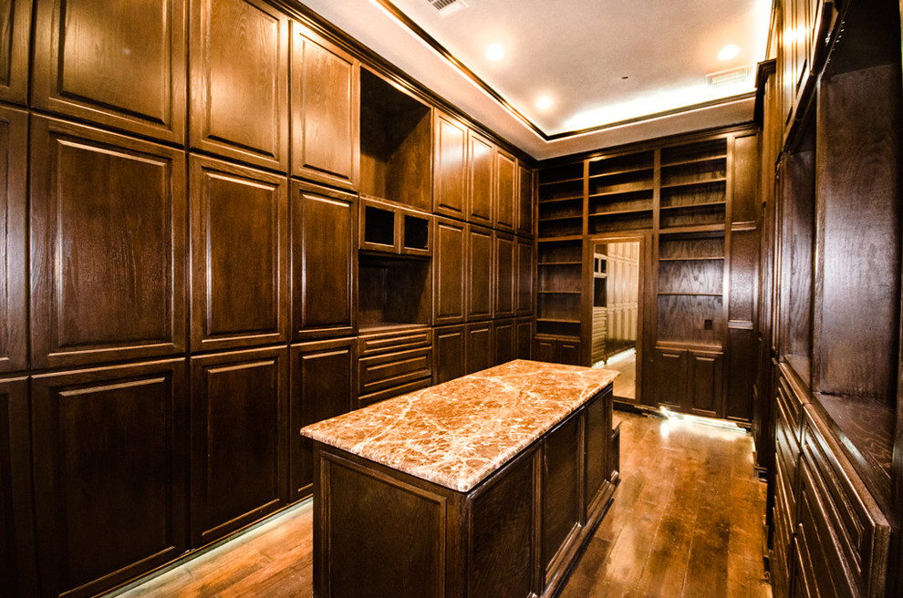 This is an example of an expansive mediterranean storage and wardrobe in Houston with flat-panel cabinets, dark wood cabinets and dark hardwood floors.