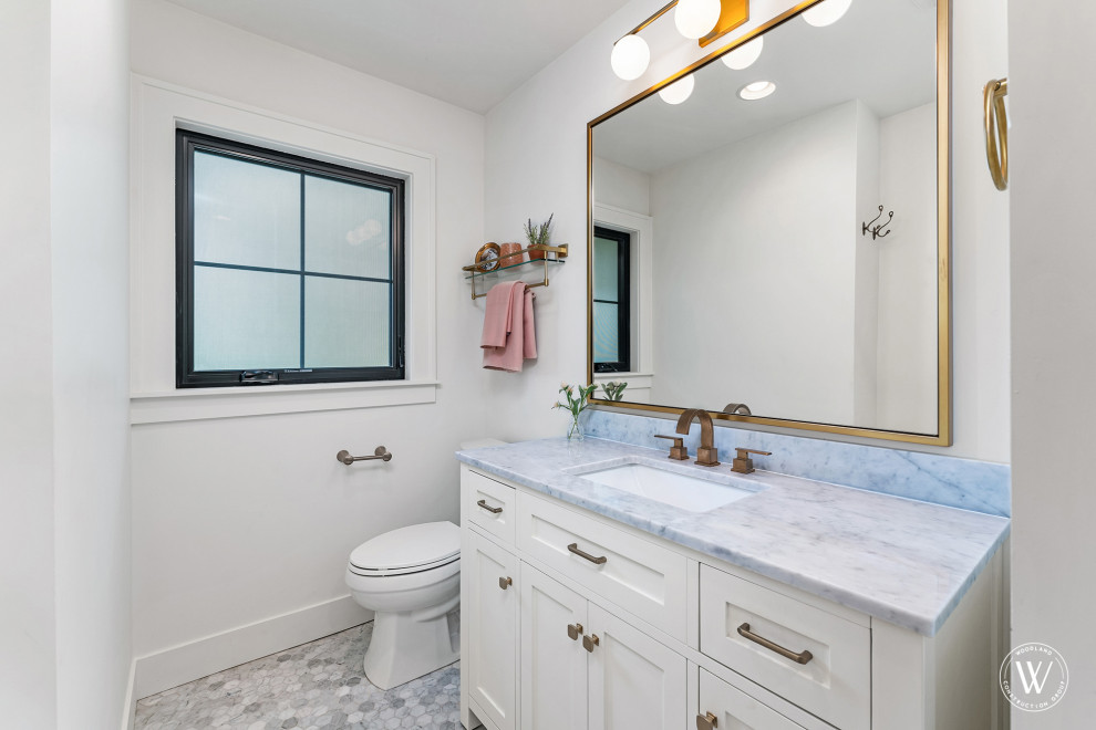 Photo of a classic bathroom with white cabinets, a built-in bath, a shower/bath combination, a two-piece toilet, white walls, marble flooring, an open shower, a single sink and a freestanding vanity unit.