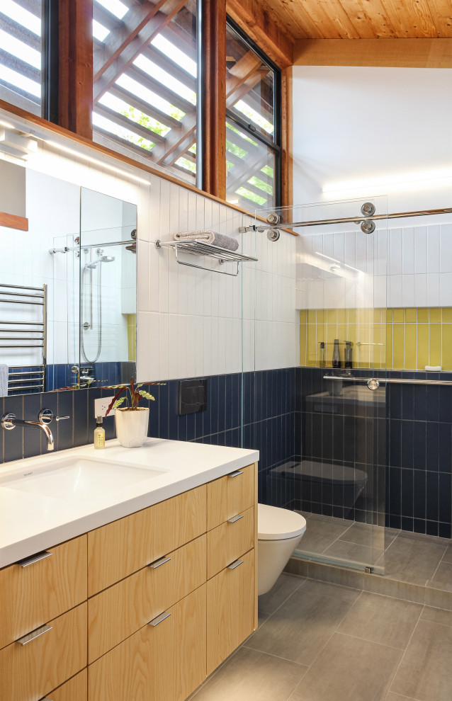 This is an example of a large midcentury master bathroom in San Francisco with flat-panel cabinets, light wood cabinets, an open shower, a wall-mount toilet, blue tile, subway tile, white walls, ceramic floors, an integrated sink, quartzite benchtops, grey floor, a sliding shower screen, white benchtops, a niche, a single vanity, a floating vanity and vaulted.