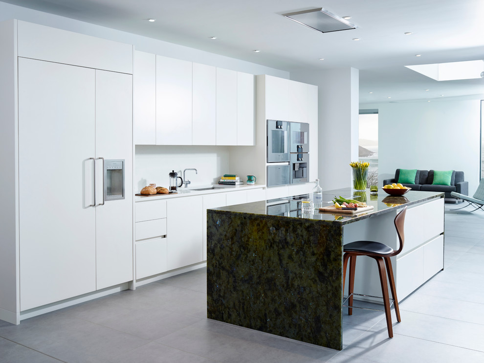 Inspiration for a contemporary galley open plan kitchen in Devon with a single-bowl sink, flat-panel cabinets, white cabinets, granite benchtops, white splashback, stainless steel appliances and with island.