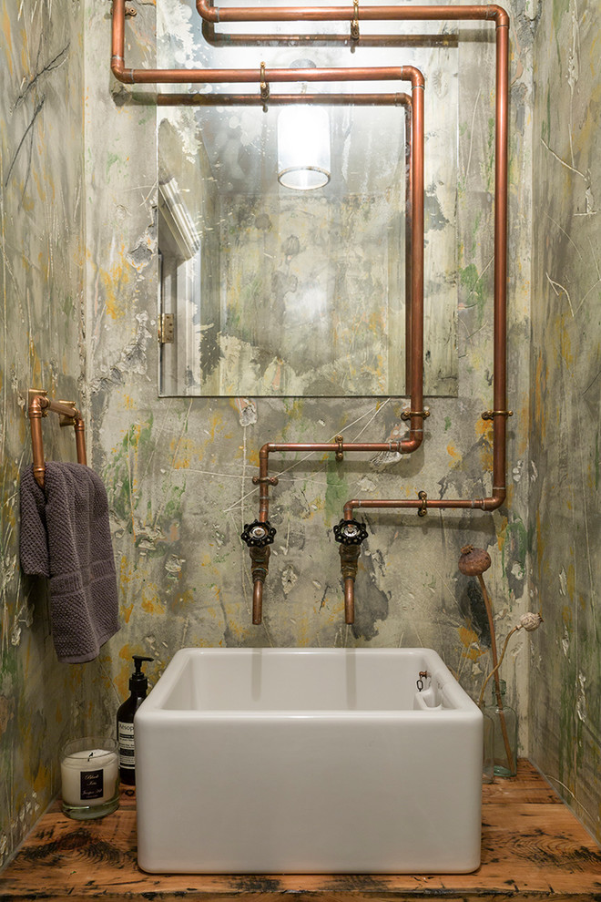 This is an example of an industrial powder room in London with green walls, a vessel sink, wood benchtops and brown benchtops.