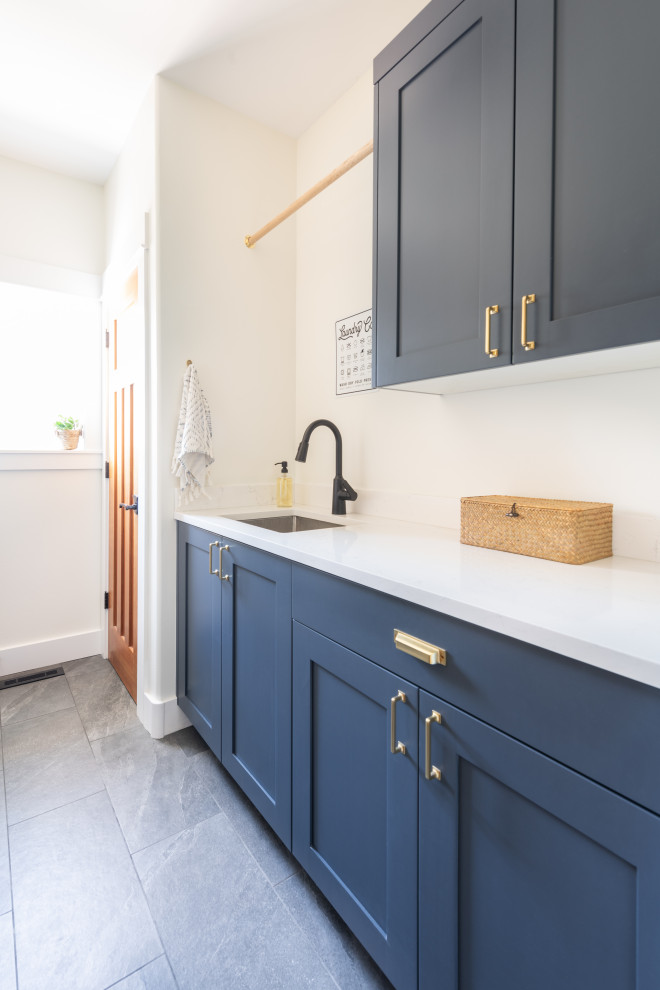 Inspiration for a small modern galley dedicated laundry room in Other with a drop-in sink, shaker cabinets, blue cabinets, quartz benchtops, white walls, porcelain floors, a side-by-side washer and dryer, grey floor and white benchtop.