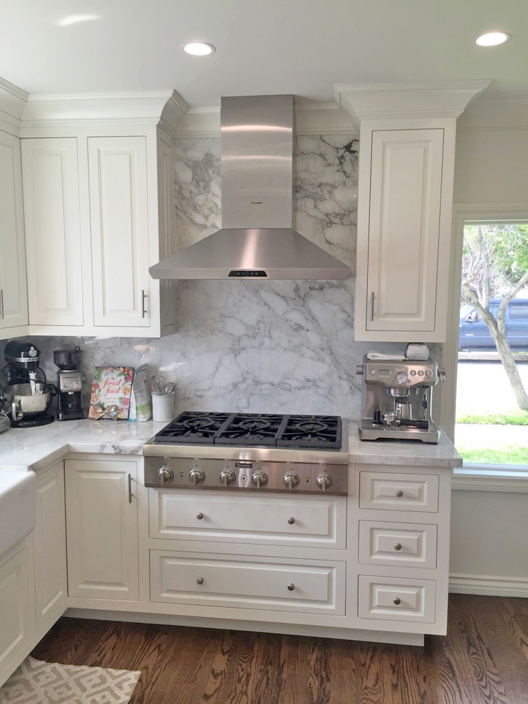 This is an example of a mid-sized traditional u-shaped separate kitchen in Los Angeles with a farmhouse sink, raised-panel cabinets, white cabinets, marble benchtops, grey splashback, marble splashback, stainless steel appliances, dark hardwood floors and brown floor.