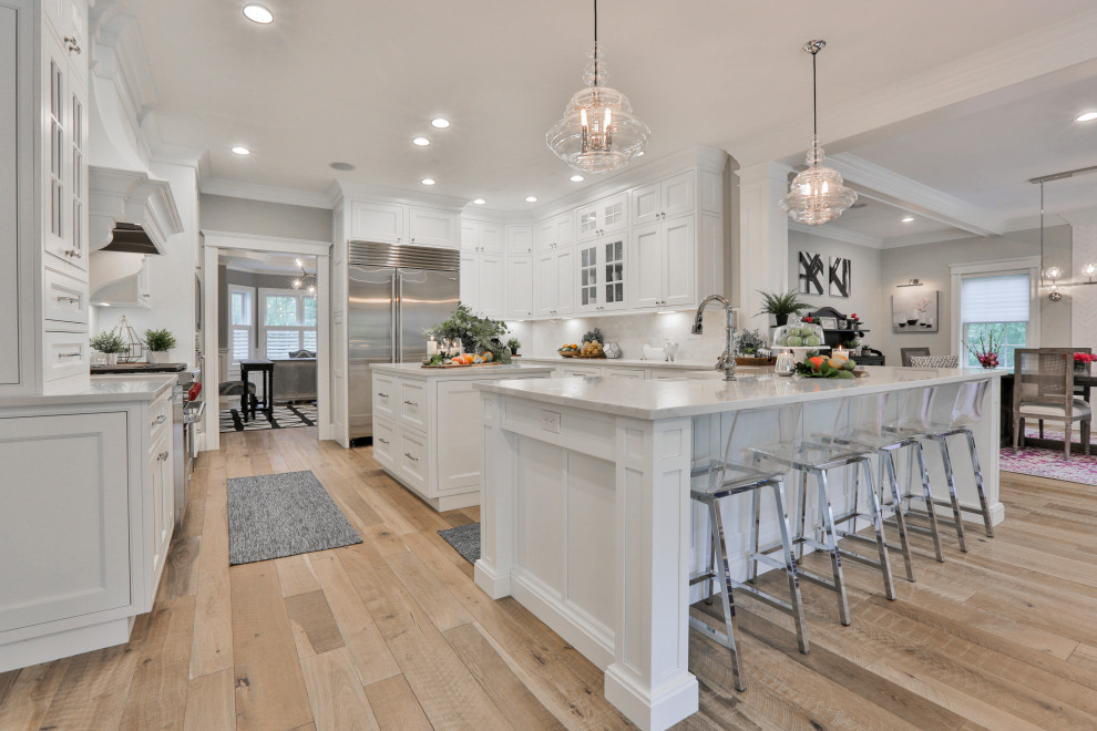 Photo of a large transitional u-shaped eat-in kitchen in Boston with a farmhouse sink, beaded inset cabinets, white cabinets, quartz benchtops, white splashback, marble splashback, stainless steel appliances, light hardwood floors, with island, multi-coloured floor and white benchtop.