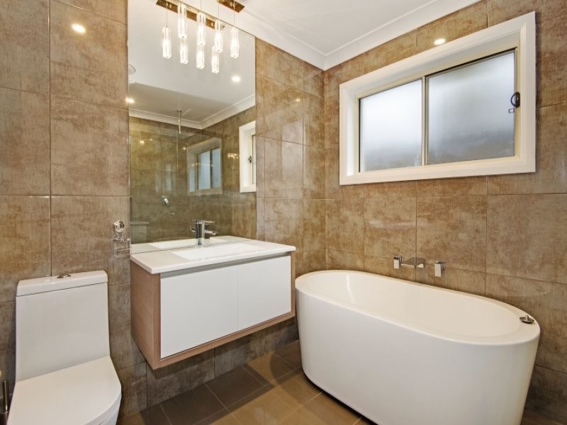 Photo of a small contemporary bathroom in Sydney with an integrated sink, flat-panel cabinets, medium wood cabinets, solid surface benchtops, a freestanding tub, a corner shower, a one-piece toilet, brown tile, porcelain tile, brown walls and porcelain floors.