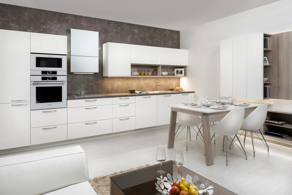 Photo of a mid-sized modern single-wall eat-in kitchen in Other with an integrated sink, flat-panel cabinets, white cabinets, laminate benchtops, brown splashback, white appliances, linoleum floors and no island.