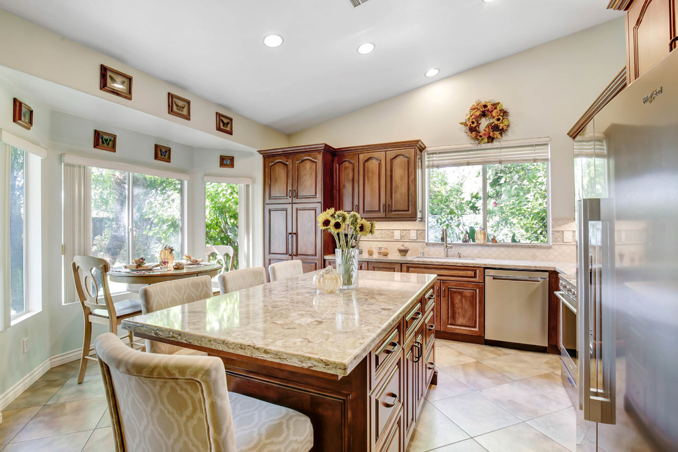 Mid-sized traditional l-shaped eat-in kitchen in Los Angeles with raised-panel cabinets, medium wood cabinets, quartz benchtops, multi-coloured splashback, travertine splashback, stainless steel appliances, porcelain floors, with island, beige floor and multi-coloured benchtop.