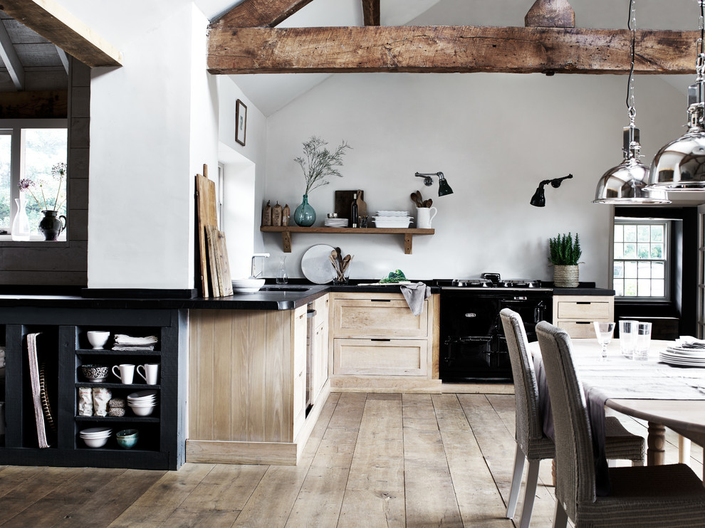 Design ideas for a large country l-shaped open plan kitchen in Dusseldorf with a farmhouse sink, shaker cabinets, light wood cabinets, white splashback, black appliances, no island and light hardwood floors.