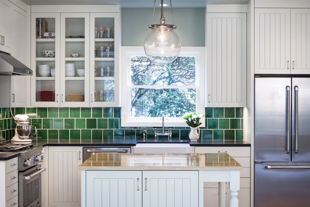 Design ideas for a mid-sized traditional u-shaped separate kitchen in Portland with a farmhouse sink, glass-front cabinets, white cabinets, granite benchtops, green splashback, ceramic splashback, stainless steel appliances, light hardwood floors and with island.