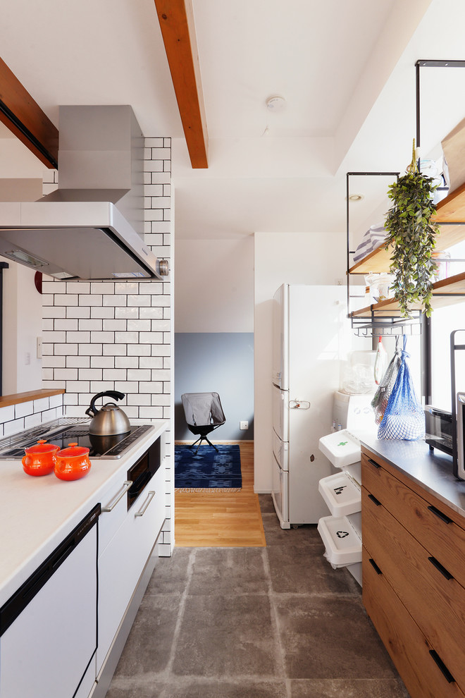 This is an example of an eclectic single-wall open plan kitchen in Tokyo with flat-panel cabinets, white cabinets, white splashback, subway tile splashback, terra-cotta floors, a peninsula, grey floor and brown benchtop.