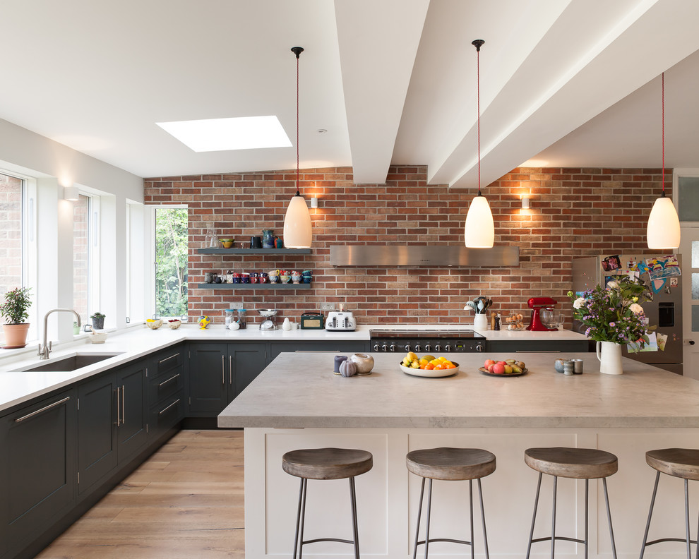 Inspiration for a large contemporary l-shaped kitchen/diner in London with a built-in sink, flat-panel cabinets, grey cabinets, concrete worktops, integrated appliances, medium hardwood flooring and a breakfast bar.