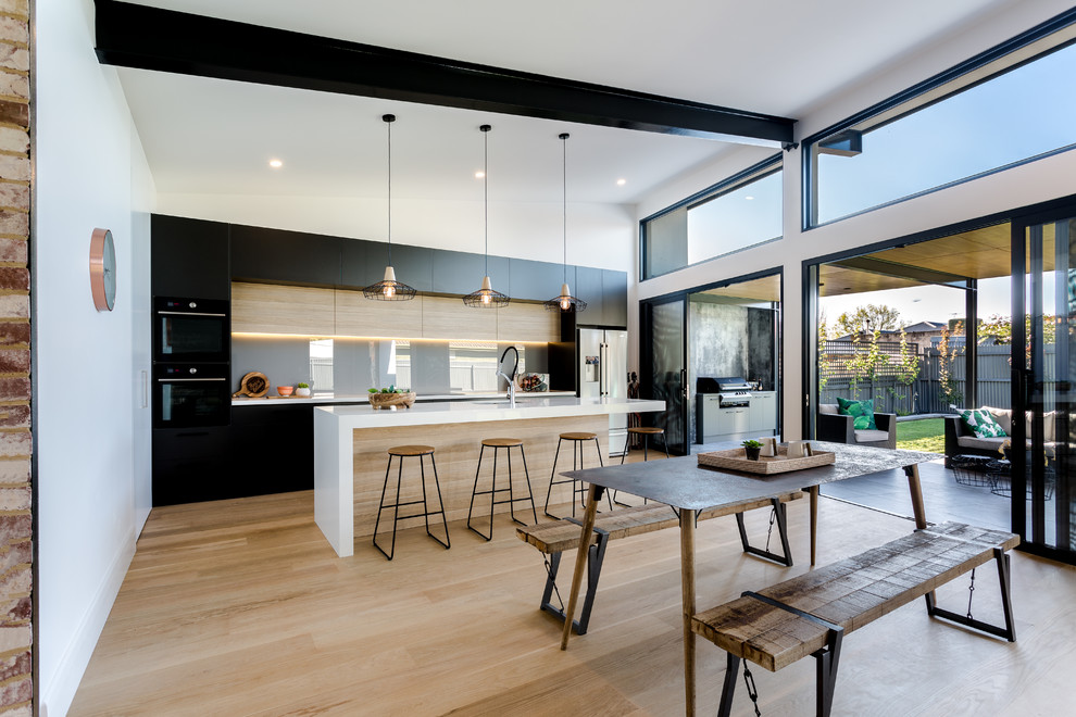 Design ideas for a large contemporary galley eat-in kitchen in Adelaide with flat-panel cabinets, glass sheet splashback, light hardwood floors, multiple islands, an undermount sink, black cabinets, grey splashback, beige floor and white benchtop.