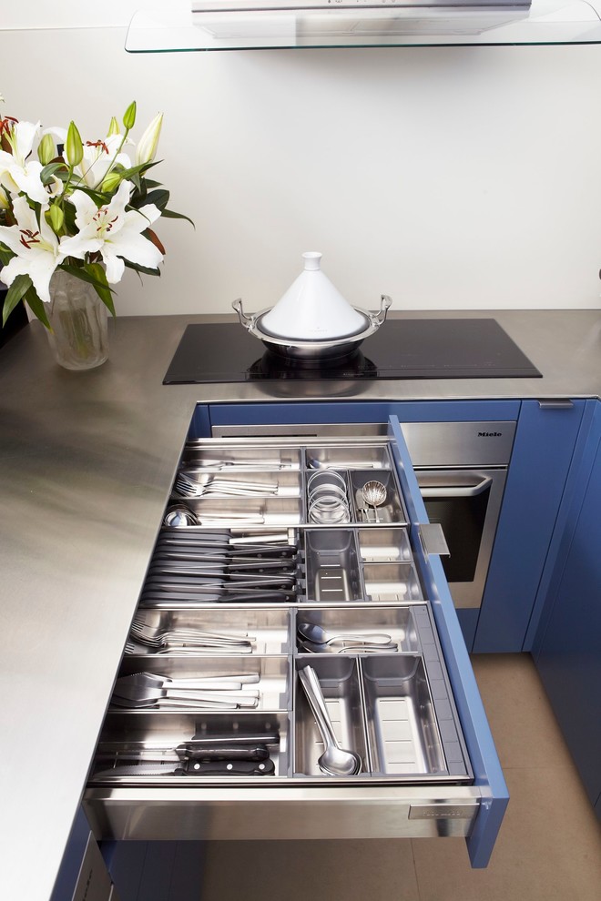 This is an example of a small contemporary u-shaped eat-in kitchen in Sydney with an integrated sink, flat-panel cabinets, blue cabinets, stainless steel benchtops, white splashback, glass sheet splashback, stainless steel appliances and porcelain floors.