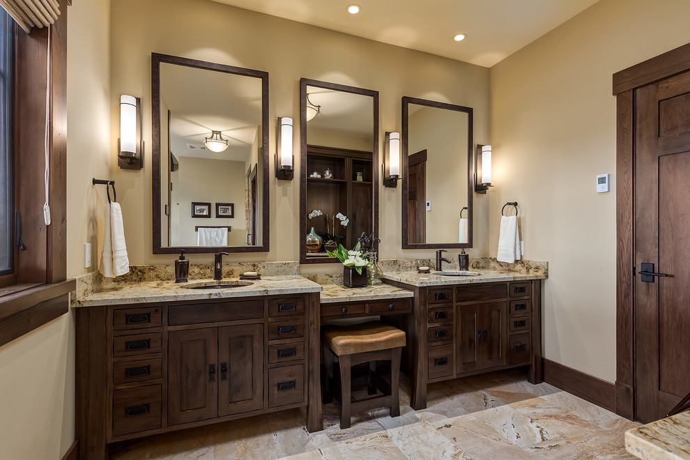 This is an example of a large arts and crafts master bathroom in Calgary with an undermount sink, dark wood cabinets, granite benchtops, beige tile, stone tile, yellow walls, travertine floors and furniture-like cabinets.