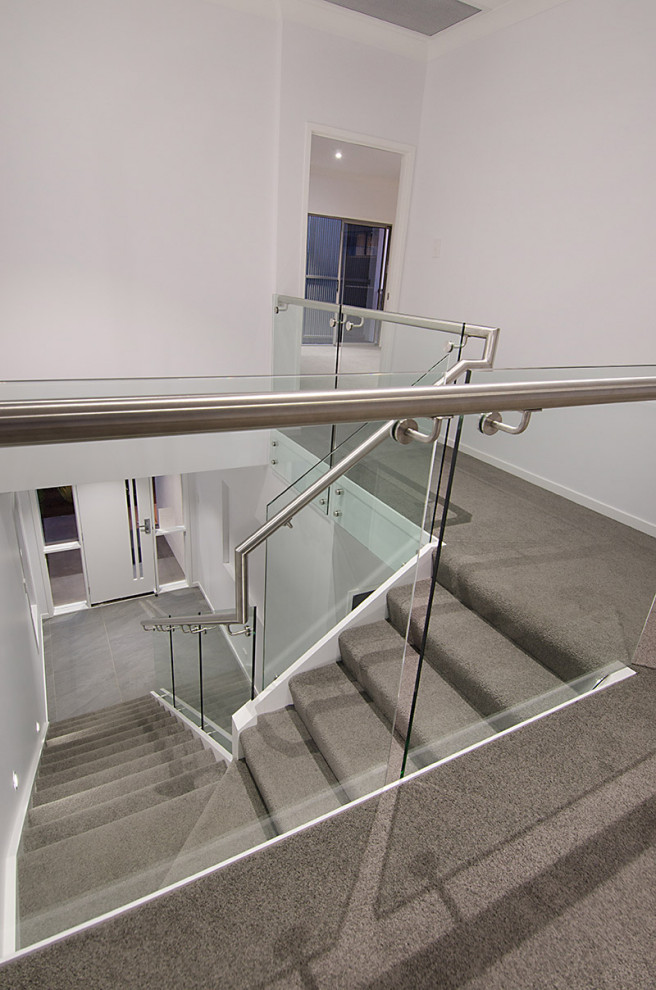 This is an example of a mid-sized modern carpeted l-shaped staircase in Brisbane with carpet risers and glass railing.
