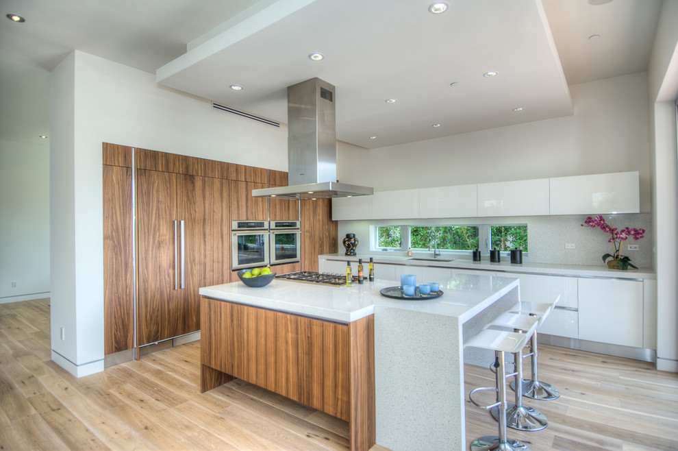 Expansive contemporary l-shaped eat-in kitchen in Los Angeles with flat-panel cabinets, white cabinets, stainless steel appliances, light hardwood floors and with island.