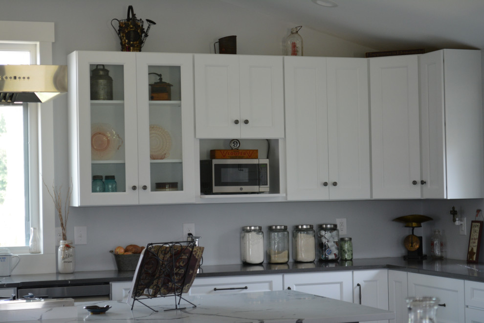 Klassisk inredning av ett mycket stort grå grått kök, med en undermonterad diskho, släta luckor, vita skåp, bänkskiva i kvarts, rostfria vitvaror, en köksö och brunt golv