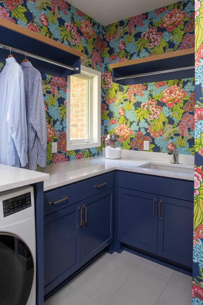 Immagine di una lavanderia classica con lavello sottopiano, ante blu, top in quarzo composito, pavimento in gres porcellanato, lavatrice e asciugatrice affiancate, top bianco e carta da parati