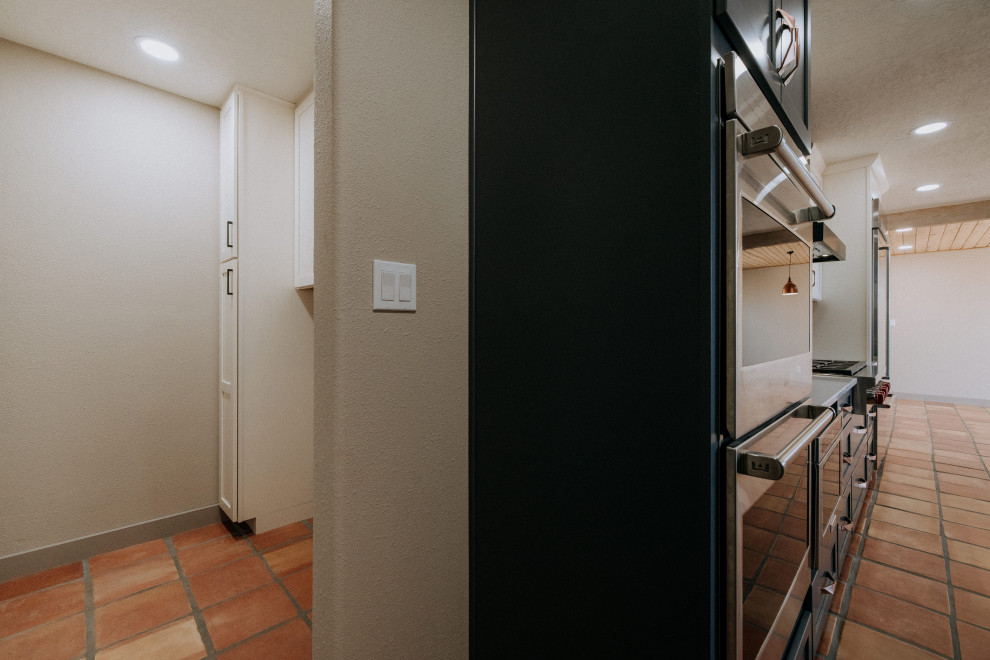 Foto di una sala lavanderia american style di medie dimensioni con ante in stile shaker, ante bianche, pavimento in terracotta, lavatrice e asciugatrice affiancate e pavimento arancione
