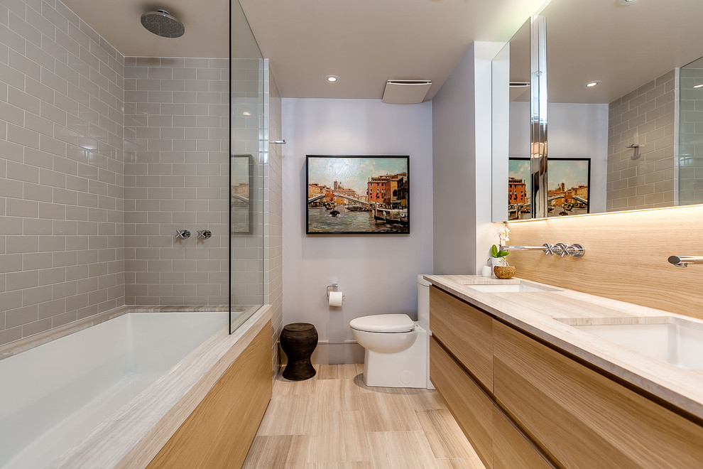 This is an example of a mid-sized contemporary master bathroom in Toronto with an undermount sink, flat-panel cabinets, light wood cabinets, marble benchtops, an undermount tub, a shower/bathtub combo, a one-piece toilet, gray tile, subway tile and grey walls.
